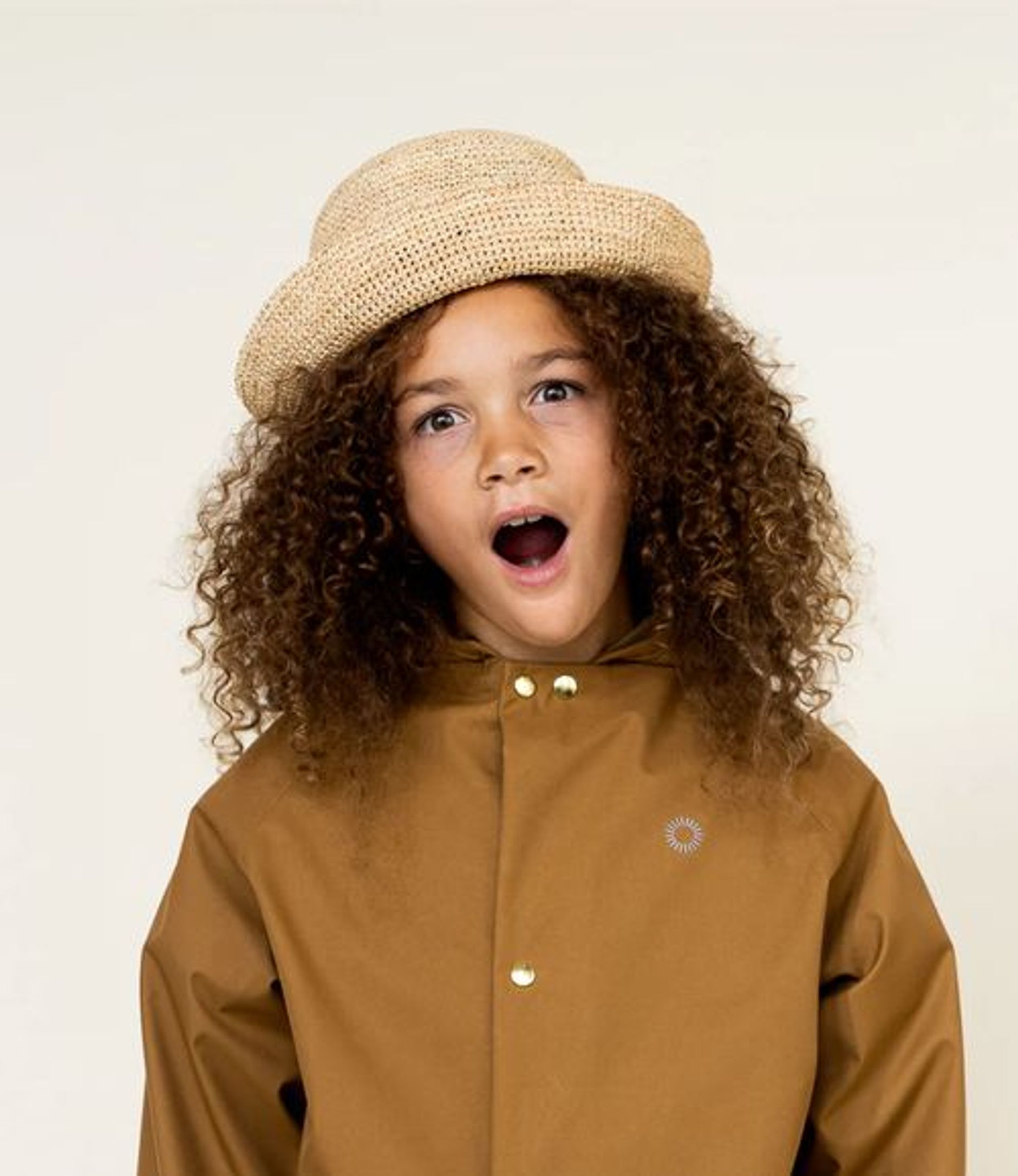 Child with curly hair wearing a hat and brown rain coat