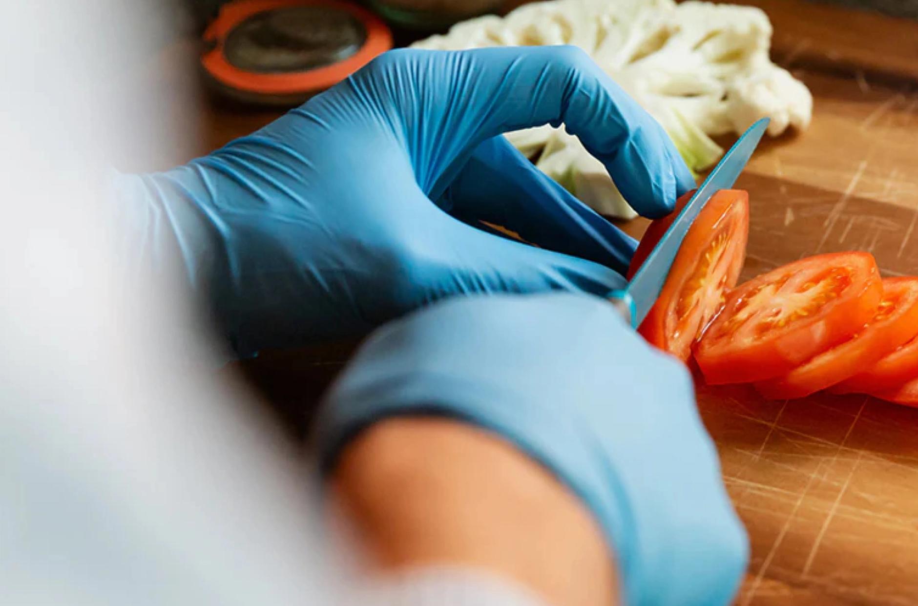 Chef with gloves on slicing tomatoes