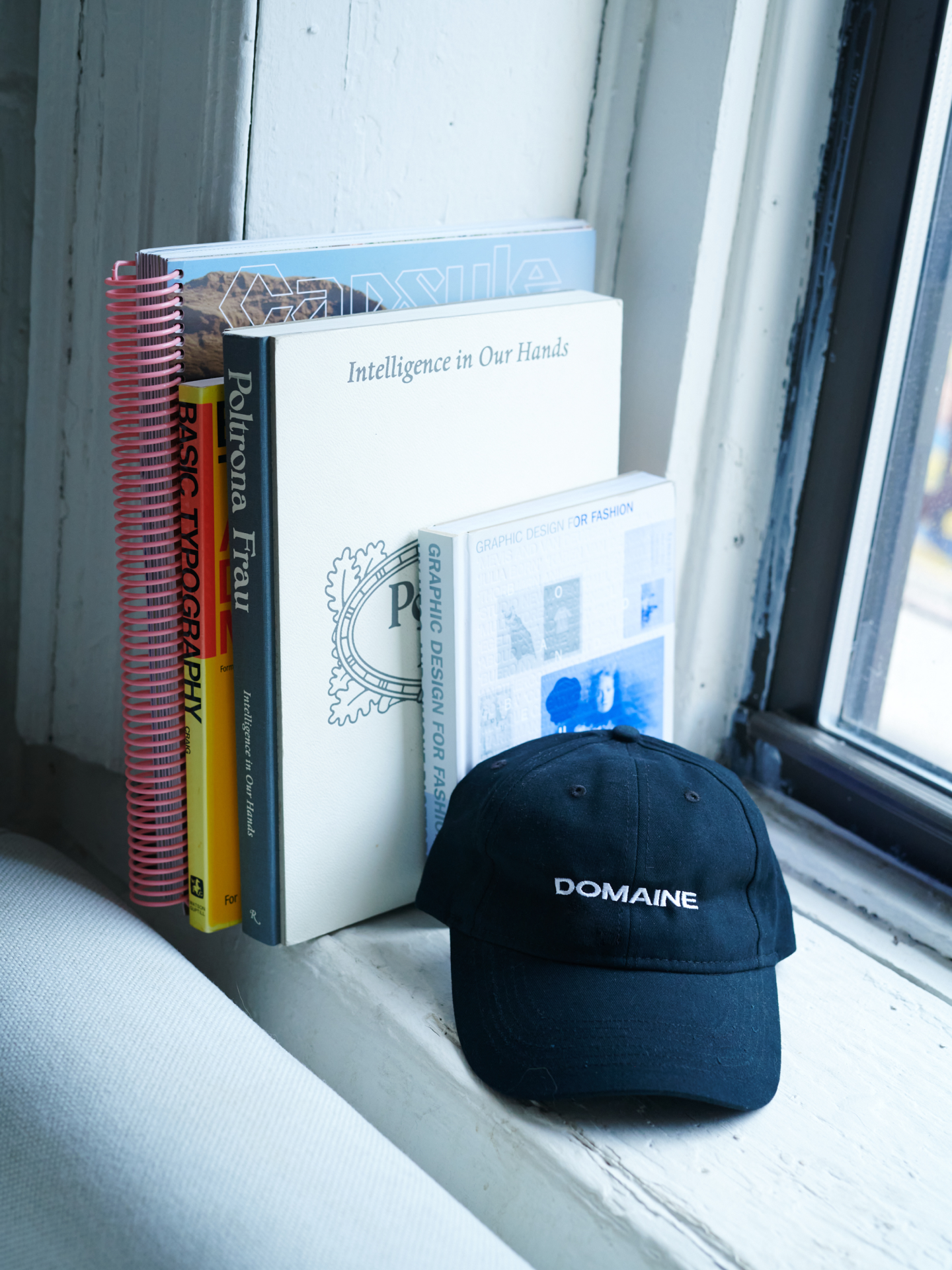 Domaine branded cap on a windowsill, behind is a number of books stacked including "intelligence in our hands" 