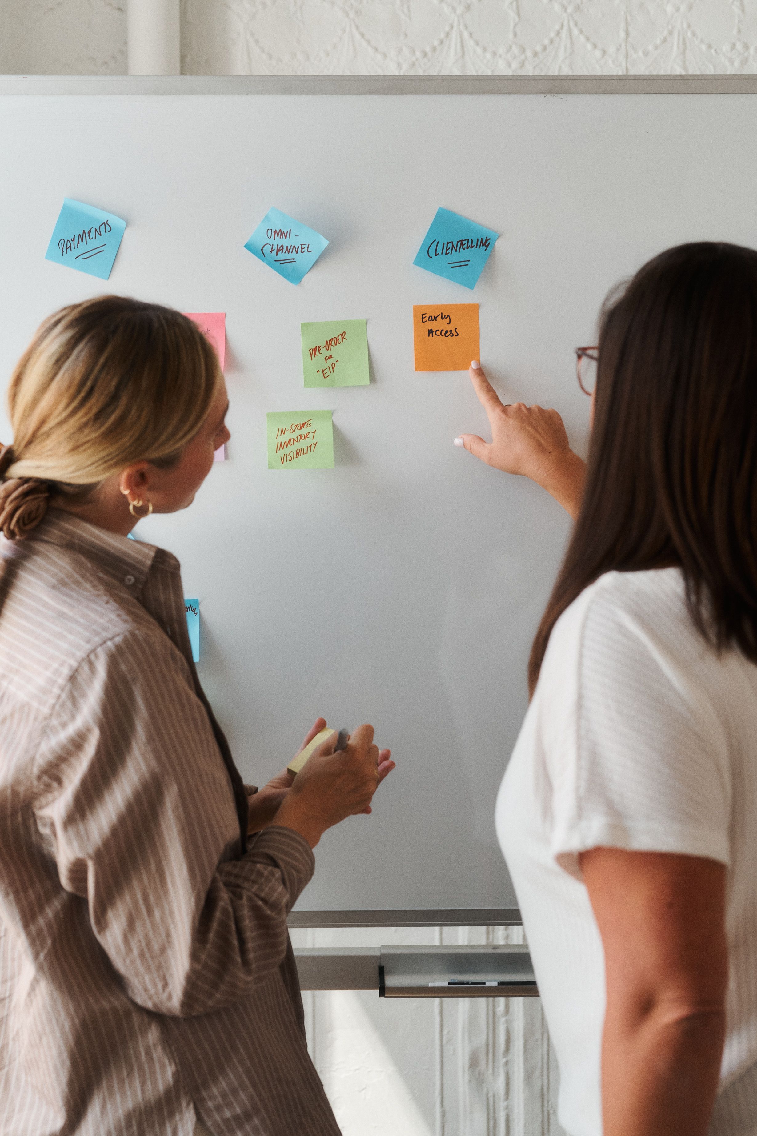 Two team members pointing at sticky notes on whiteboard