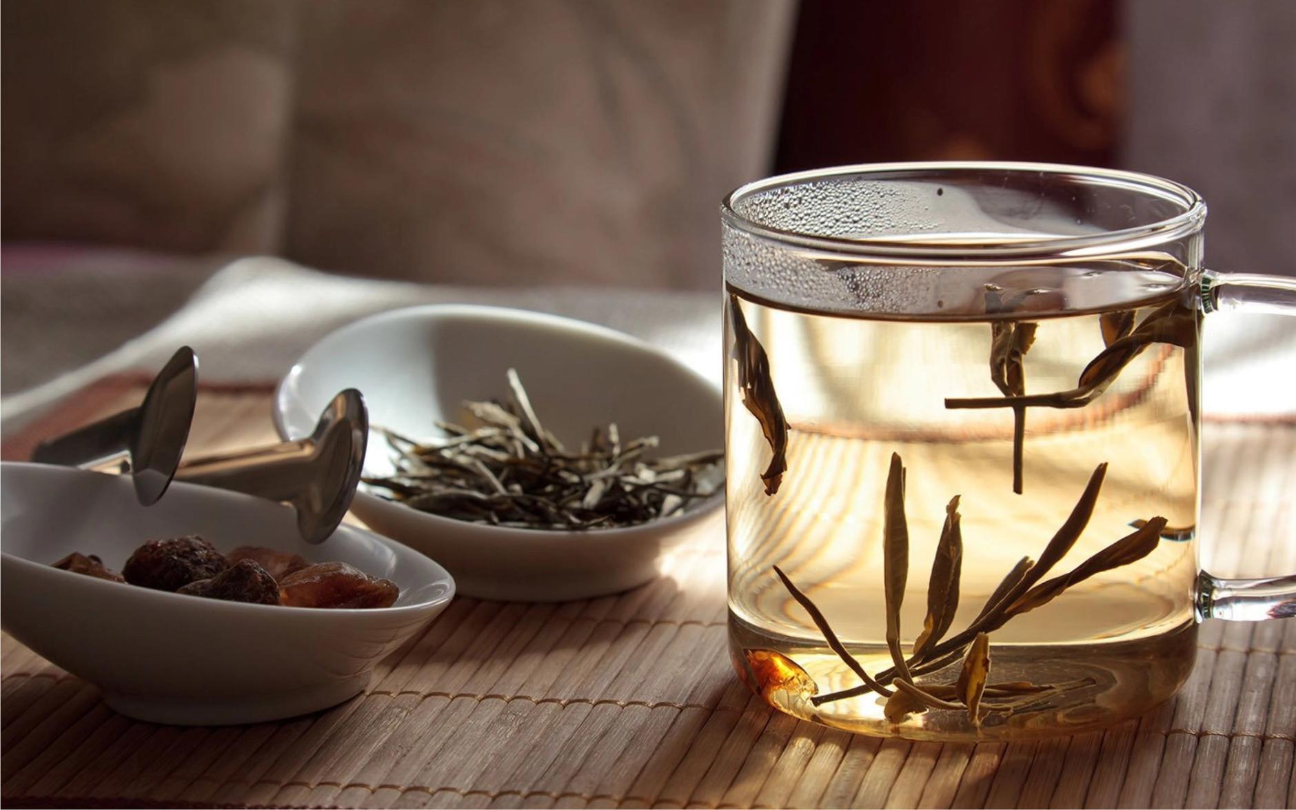 Glass mug of tea next to bowls of tea leaves on table