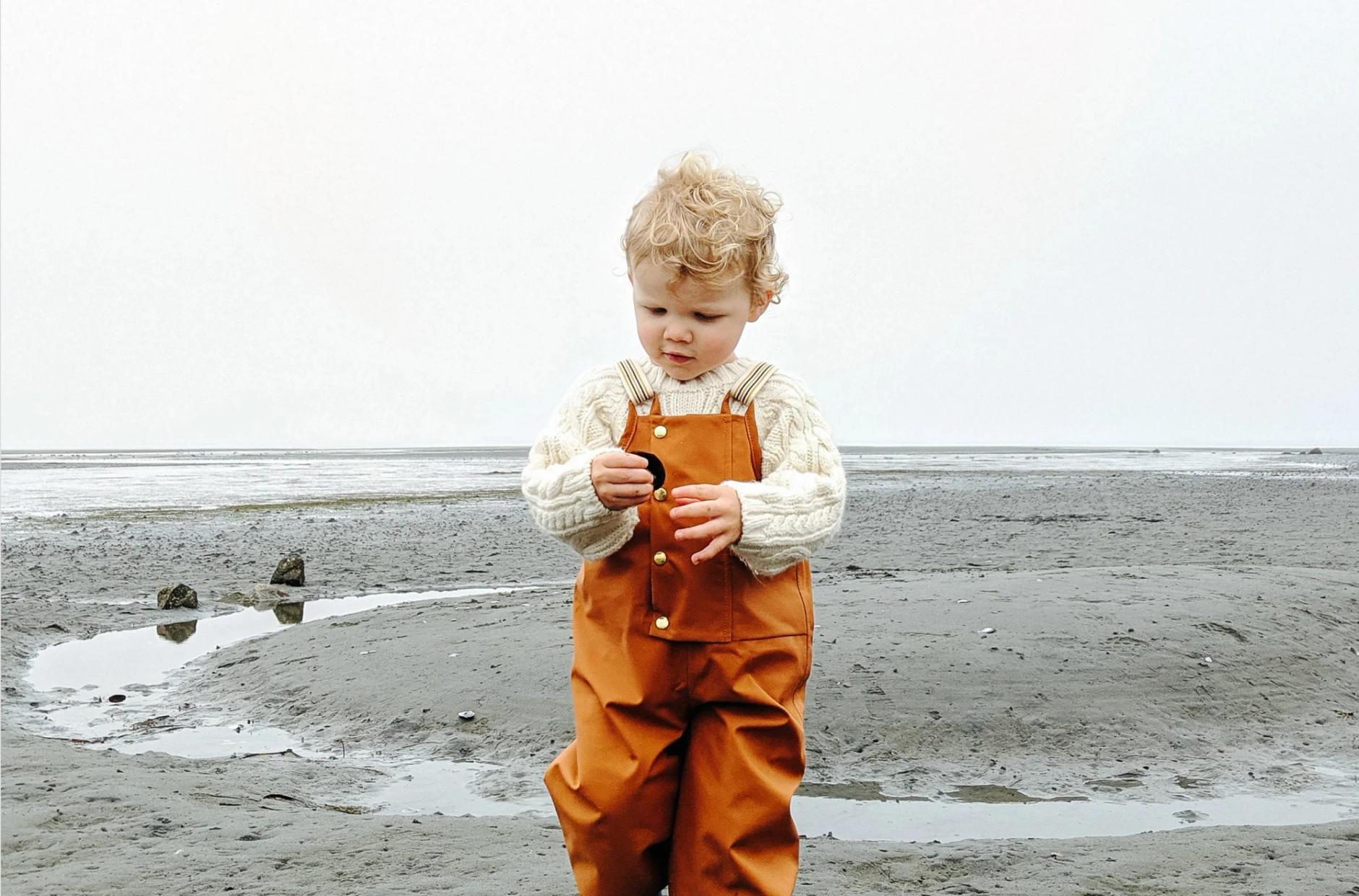Small child on beach in overalls