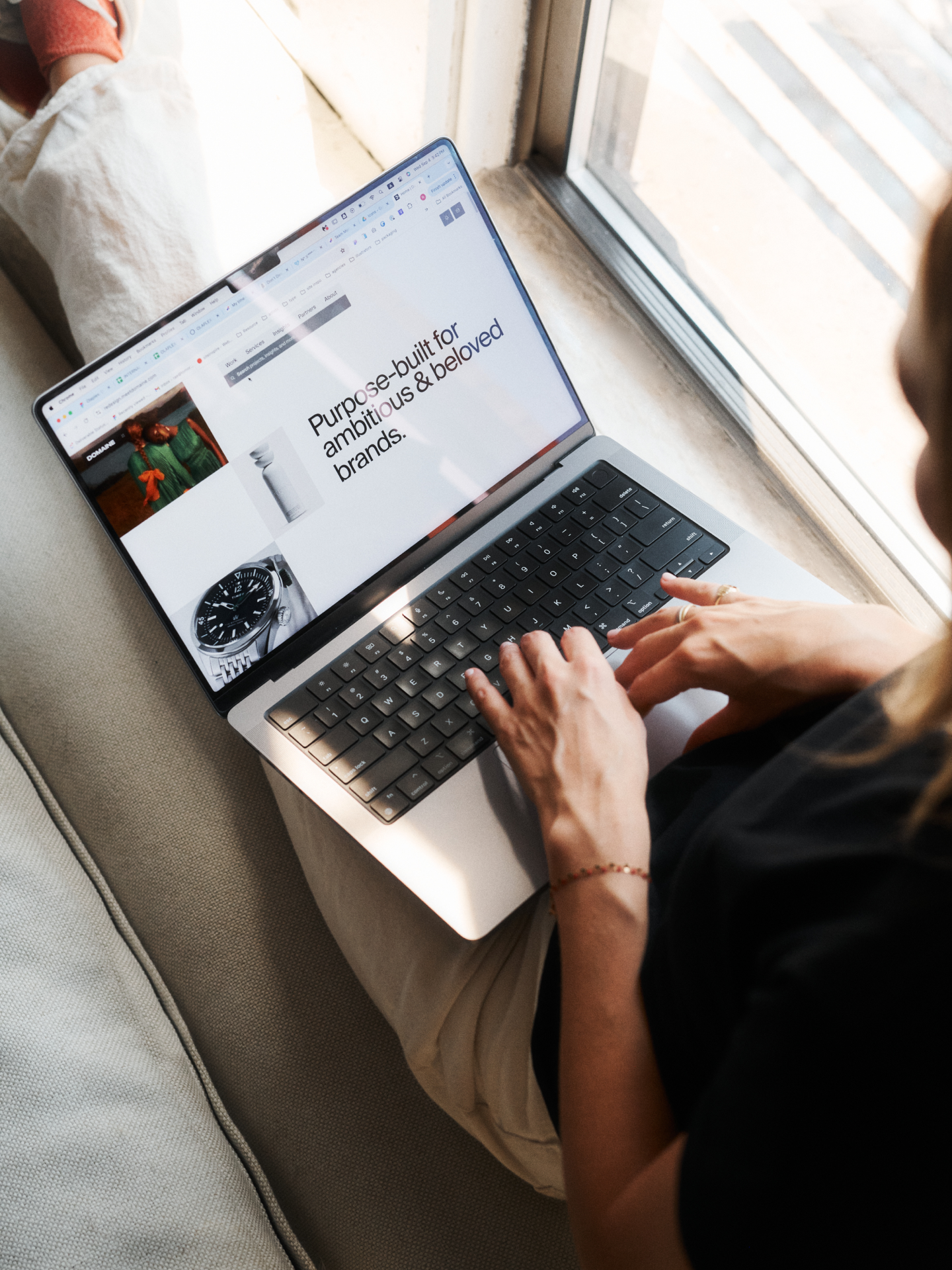 Lenora sitting on a window ledge with a laptop open showing the Domaine website