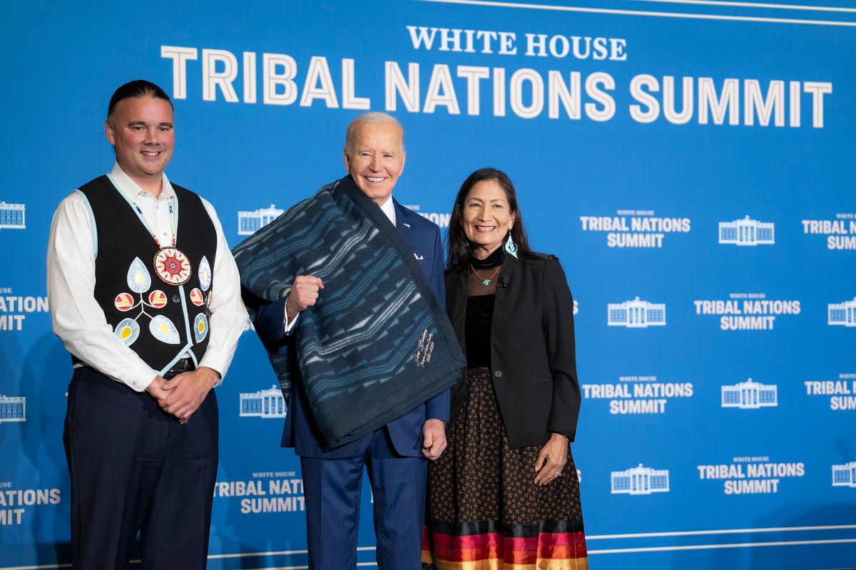 The US Secretary of the Interior Deb Haaland (right) and Assistant Secretary for Indian Affairs Bryan Newland (left) present a ceremonial blanket to President Joe Biden at the Tribal Nations Summit, 9 December 2024, at the Department of the Interior in Washington, DC. Official White House Photo by Adam Schultz, via Flickr