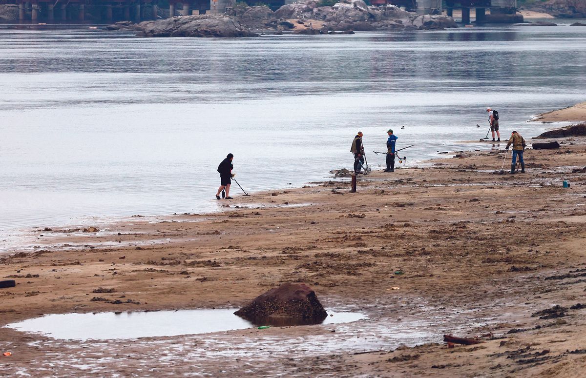 Local residents use metal detectors to search the muddy banks exposed by the receding waters of the Dnipro river on the central beach of Zaporizhzhia, following the Nova Kakhovka dam breach. Ukrainian officials have urged residents to report displaced artefacts