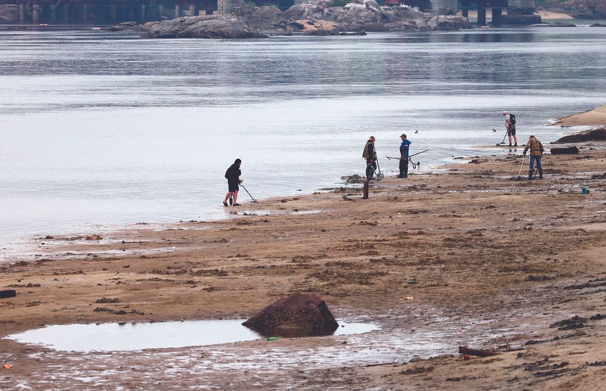 Local residents use metal detectors to search the muddy banks exposed by the receding waters of the Dnipro river on the central beach of Zaporizhzhia, following the Nova Kakhovka dam breach. Ukrainian officials have urged residents to report displaced artefacts