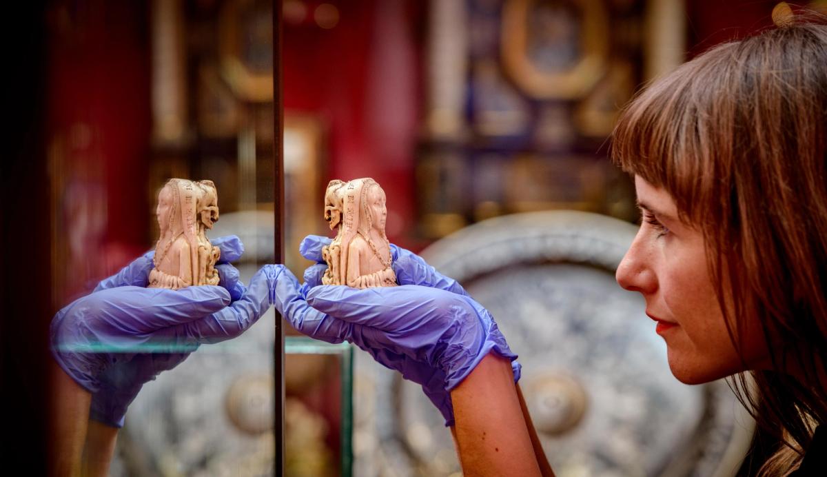 A curator with a small ivory pendant produced in the Netherlands in around 1500. The work is known as an example of a memento mori, or ‘remember death’ in Latin—it juxtaposes life and death to remind its owner to live a life free of sin

© English Heritage Trust