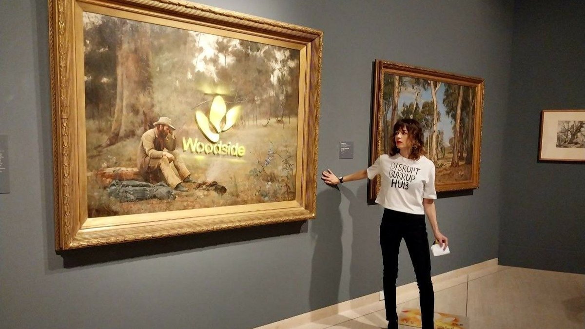 A protestor stands in front of the Frederick McCubbin painting Down on his luck which was spray painted at the Art Gallery of Western Australia in January 2023
Photograph: Disrupt Burrup Hub