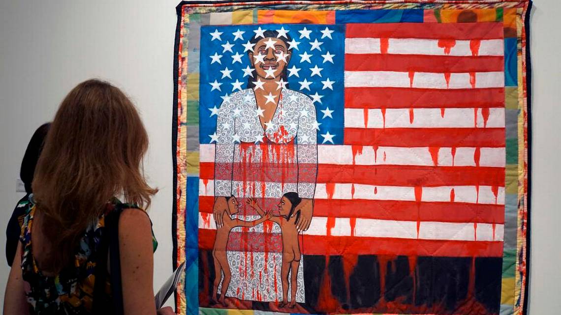 A fair-goer looks at the work of US artist Faith Ringgold, “The Flag is Bleeding 2” (1997), during a preview day of Art Basel in Miami Beach in 2019. Shutterstock