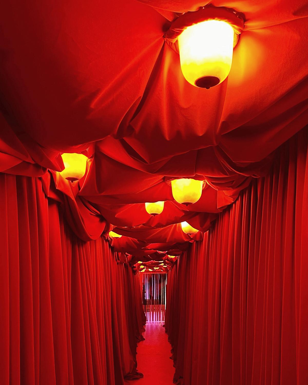 Booby Trap, an installation by Buchanan Studio featuring a hallway draped in thick velvet—and a ceiling featuring 35 “breast lights”—welcomes visitors to the Breasts exhibition at Palazzo ACP Franchetti