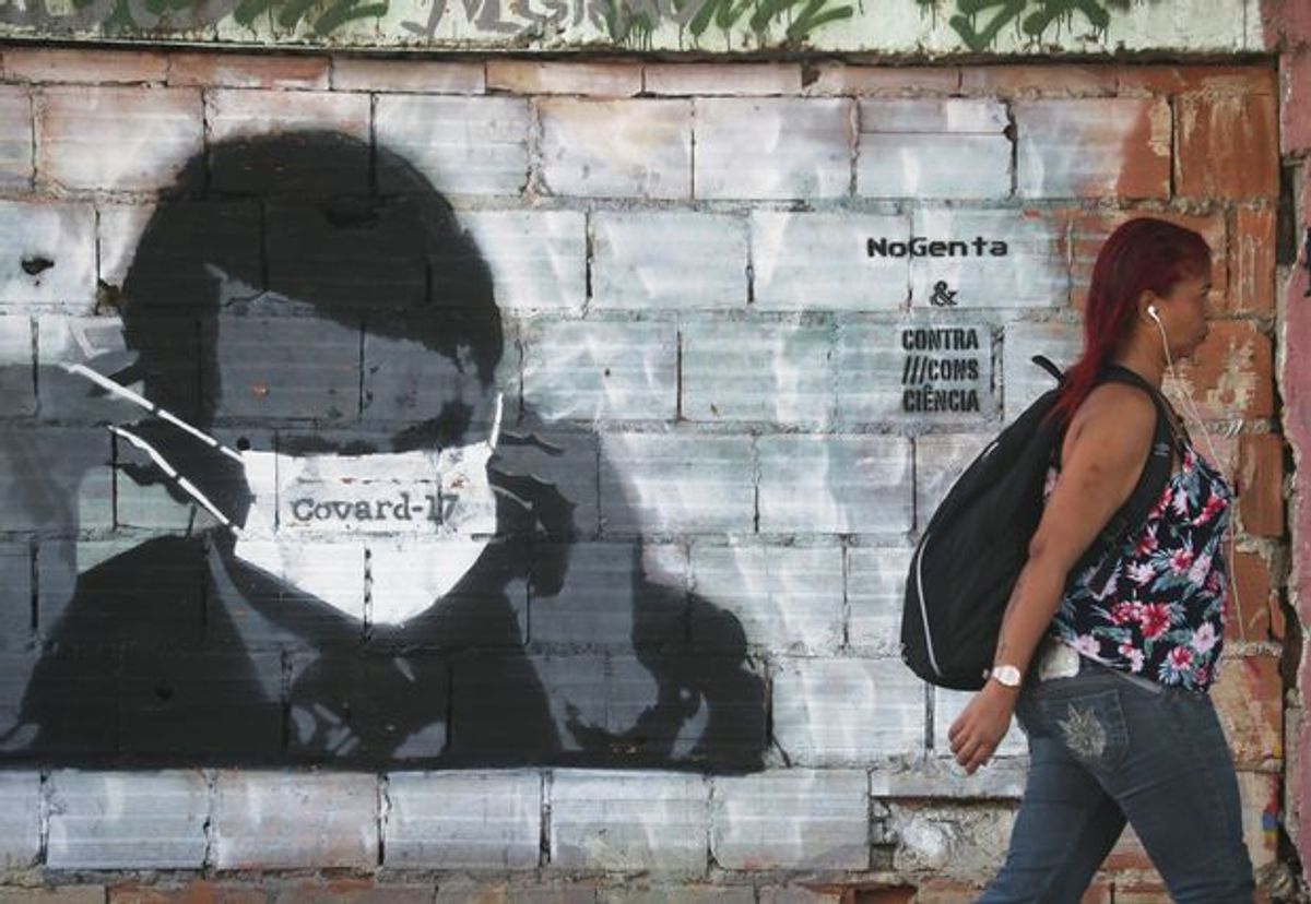 A woman walks past street art in Rio de Janeiro depicting Brazilian president Bolsonaro adjusting his protective face mask, marked ‘Coward-17’ in Portuguese. The number 17 is a reference to Bolsonaro's political party number. Sergio Moraes/Reuters