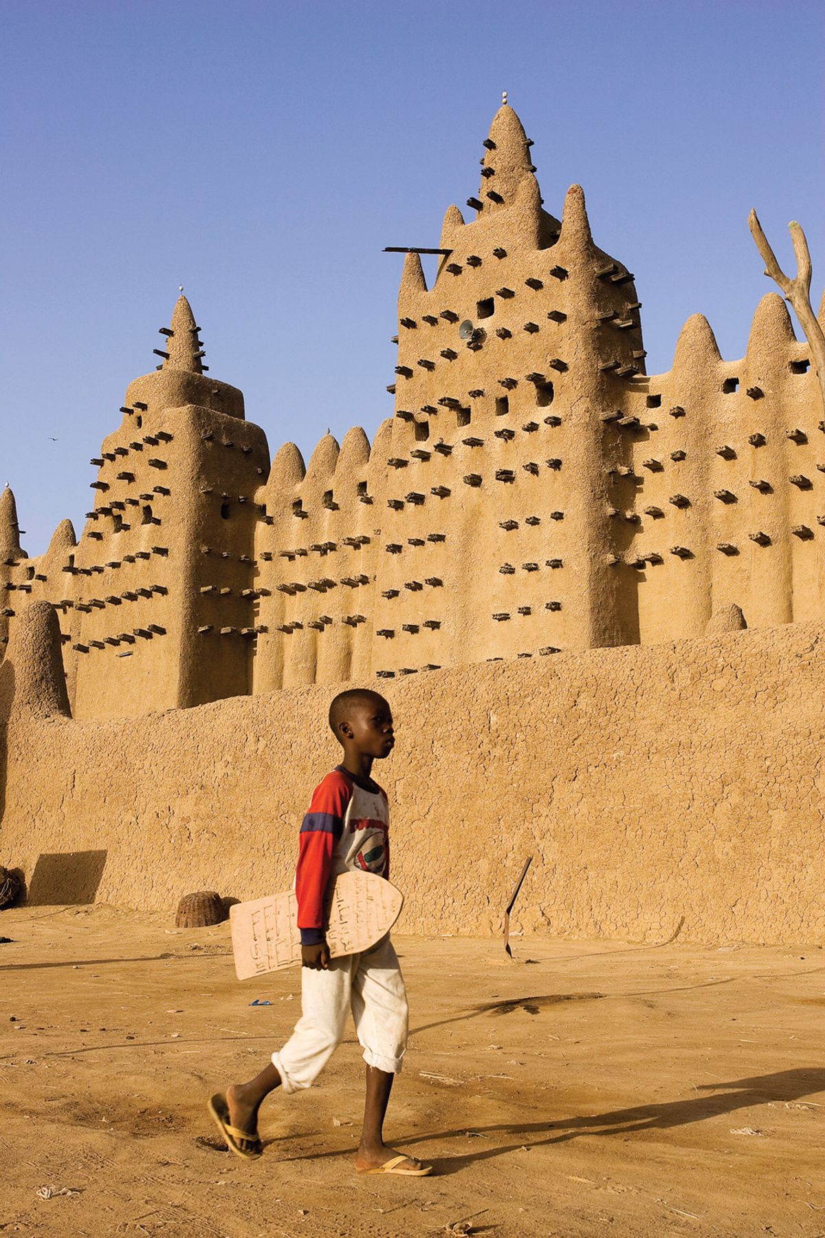 A boy carrying a lawh (wooden board on which he has written Qur’anic verses) walks past the Grand Mosque of Mopti, Mali Hemis/Alamy Stock Photo