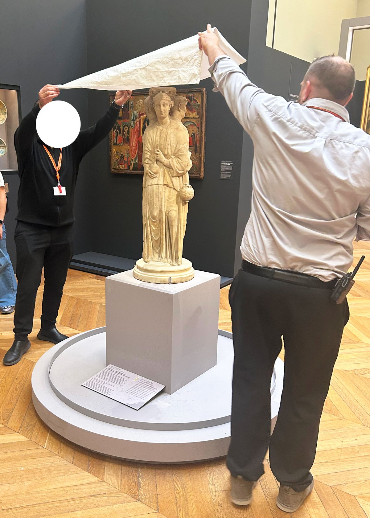 Louvre security staff hold a tarpaulin over Three Acolytes (1264-67), by the studio of the sculptor Nicola Pisano, to try to protect it from a roof leak (water damage is clearly visible in the corner of the label); museum workers' faces have been concealed out of respect for their privacy © The Art Newspaper