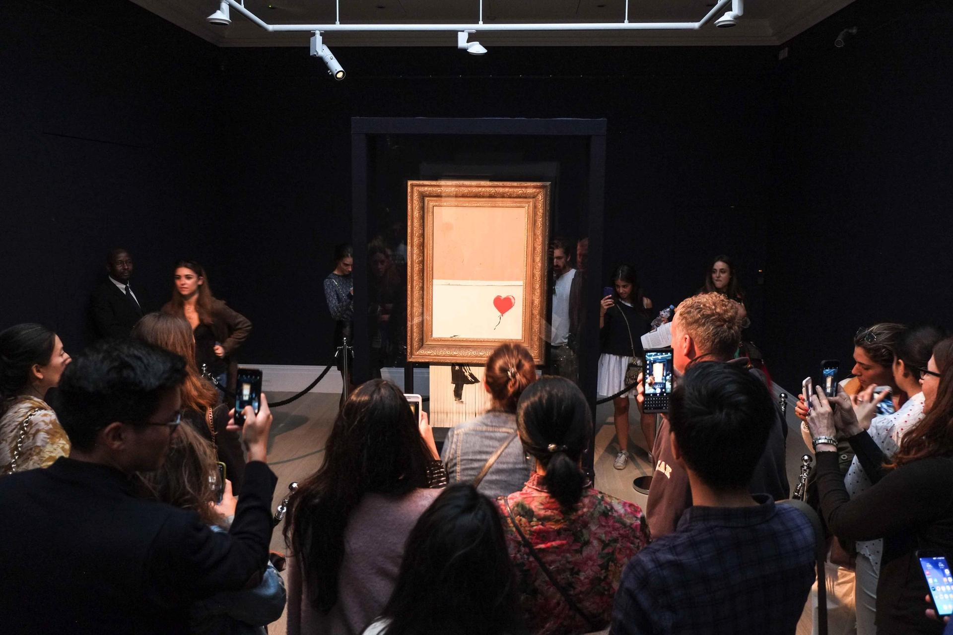 Visitors view Banksy's artwork tilted Love is in the Bin previously known as—Girl with Balloon at Sotheby's © Claire Doherty/Alamy Live News