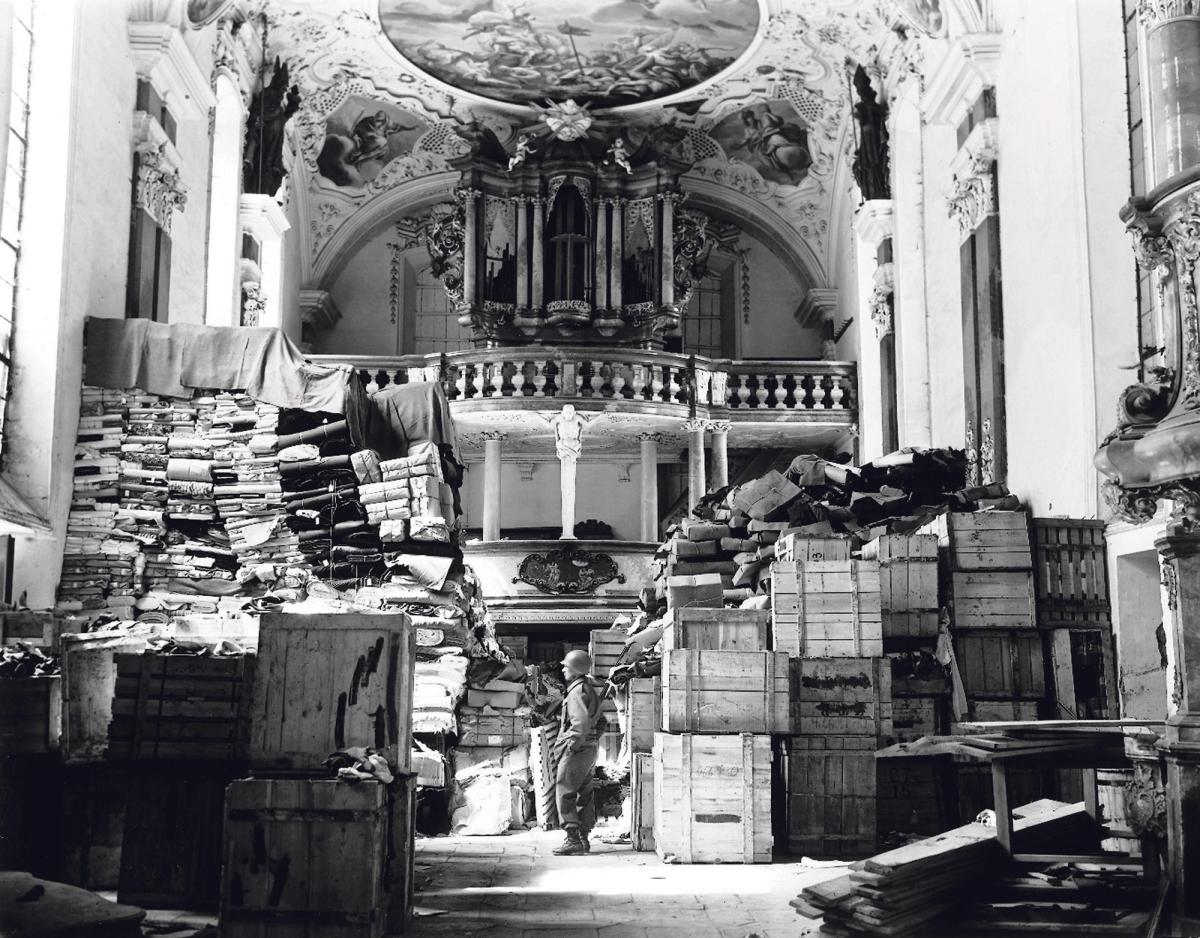 Boxes, records and clothing are guarded by a US soldier at a church in Ellingen, Germany, a Nazi depot for goods seized in France and the Netherlands NARA/Public Domain