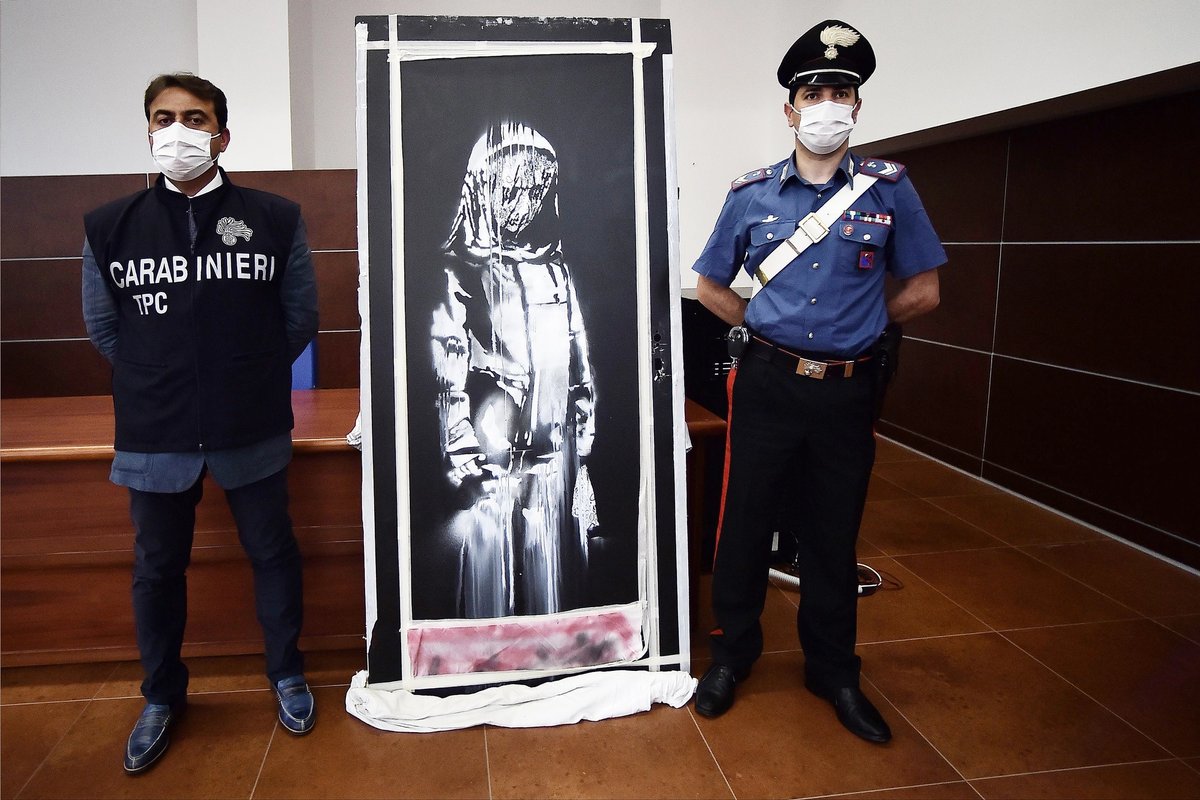 The Italian Carabinieri pose near a piece of art attributed to Banksy, that was stolen at the Bataclan in Paris in 2019, and found in Italy. Photo: Filippo Monteforte / AFP via Getty Images