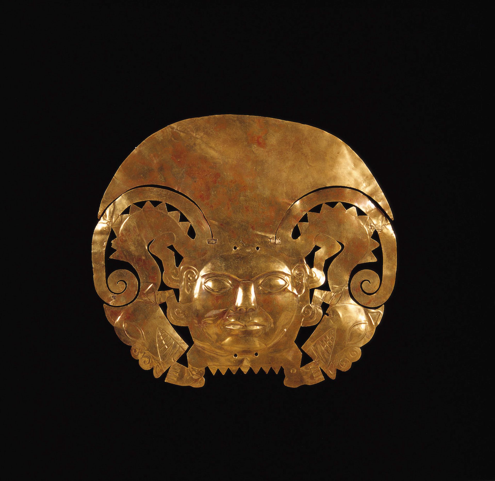 A 14-karat gold frontal adornment depicting a human head with half-moon headdress and zoomorphic figures with feline heads and appendages on the snout Museo Larco