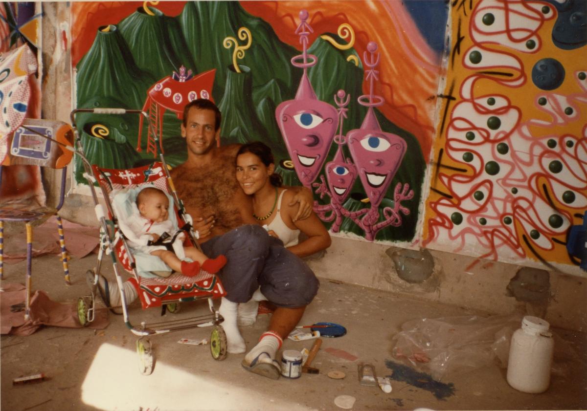 Kenny Scharf with his daughter, Zena, and wife, Tereza, in 1984, posing in front of Scharf’s artwork in Bahia, Brazil as seen in Kenny Scharf: When Worlds Collide, directed by Malia Scharf and Max Basch. A Greenwich Entertainment release Photo: Oliver Sanchez