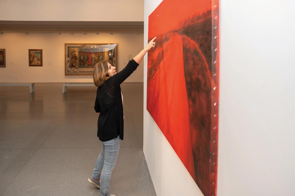 Artist Ziva Jelin points to a bullet-hole in her painting The Curving Road, part of damage it suffered on 7 October Photo: Zohar Shemesh, courtesy Israel Museum, Jerusalem