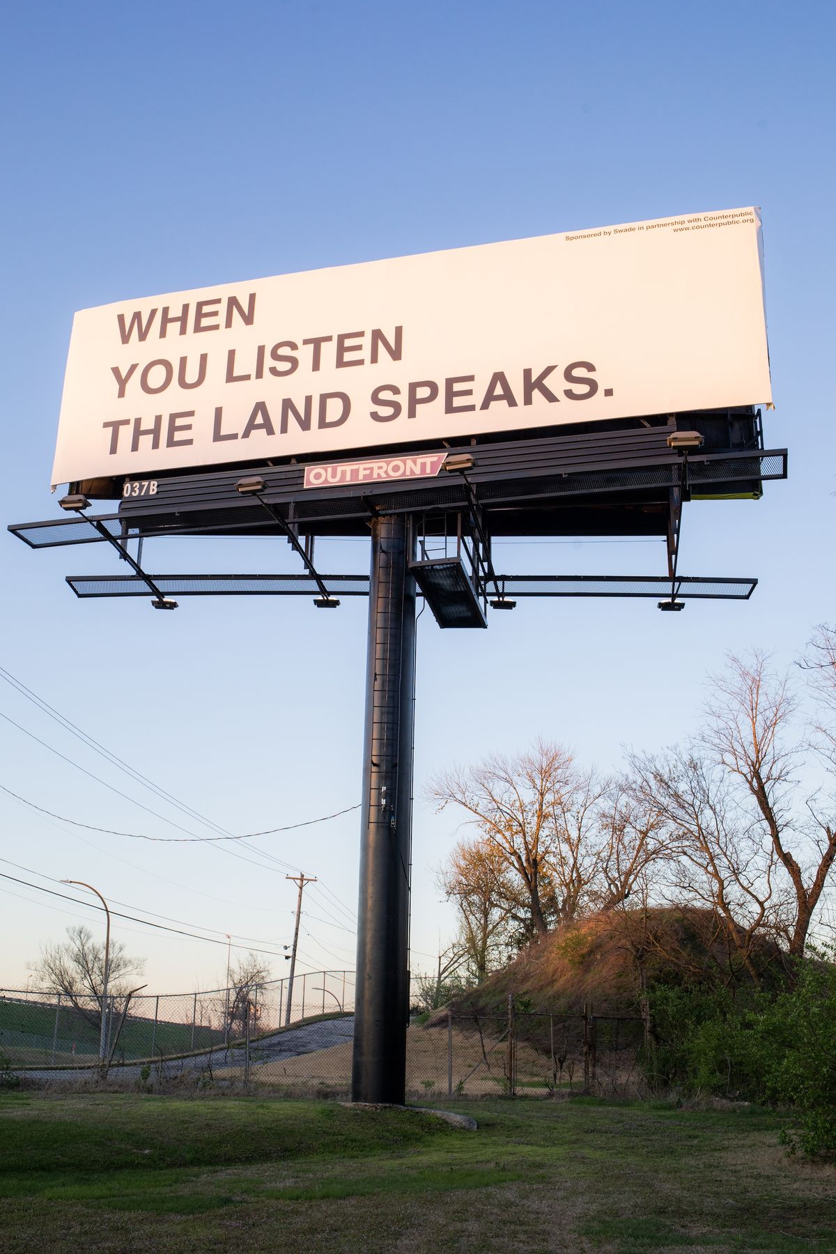 Anna Tsouhlarakis's billboard, The Native Guide Project: STL (2023), in front of the Sugarloaf Mound Photo: Chris Bauer. Commissioned by Counterpublic 2023