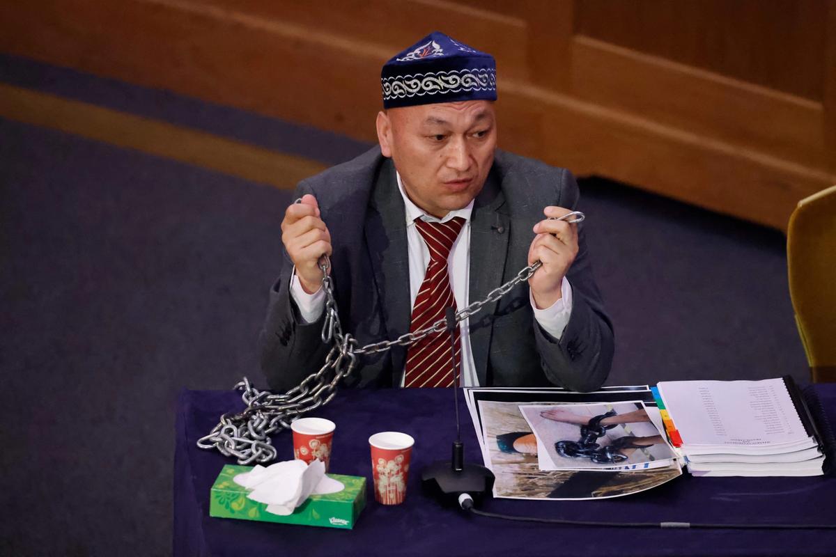 Kazakh-Uyghur witness Omir Bekali demonstrates how he was shackled in chains at a detention camp in Xinjiang as he speaks on the first day of hearings at the Uyghur Tribunal Photo: Tolga Akmen / AFP via Getty Images