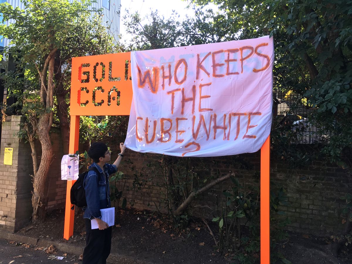 One of the protesters adjusts the "Who Keeps the Cube White" banner, obscuring the Goldsmiths CCA sign © The Art Newspaper; José da Silva