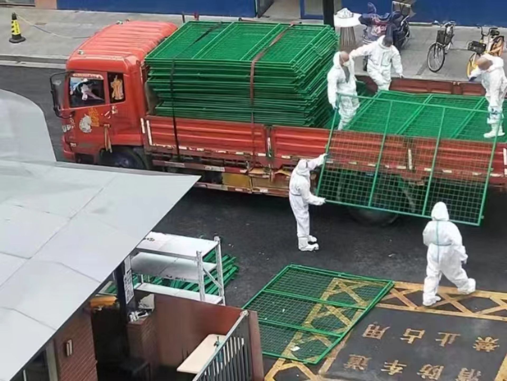 White hazmat-suited workers known as dabai, unloading metal fences to place over the doors of residences in Shanghai