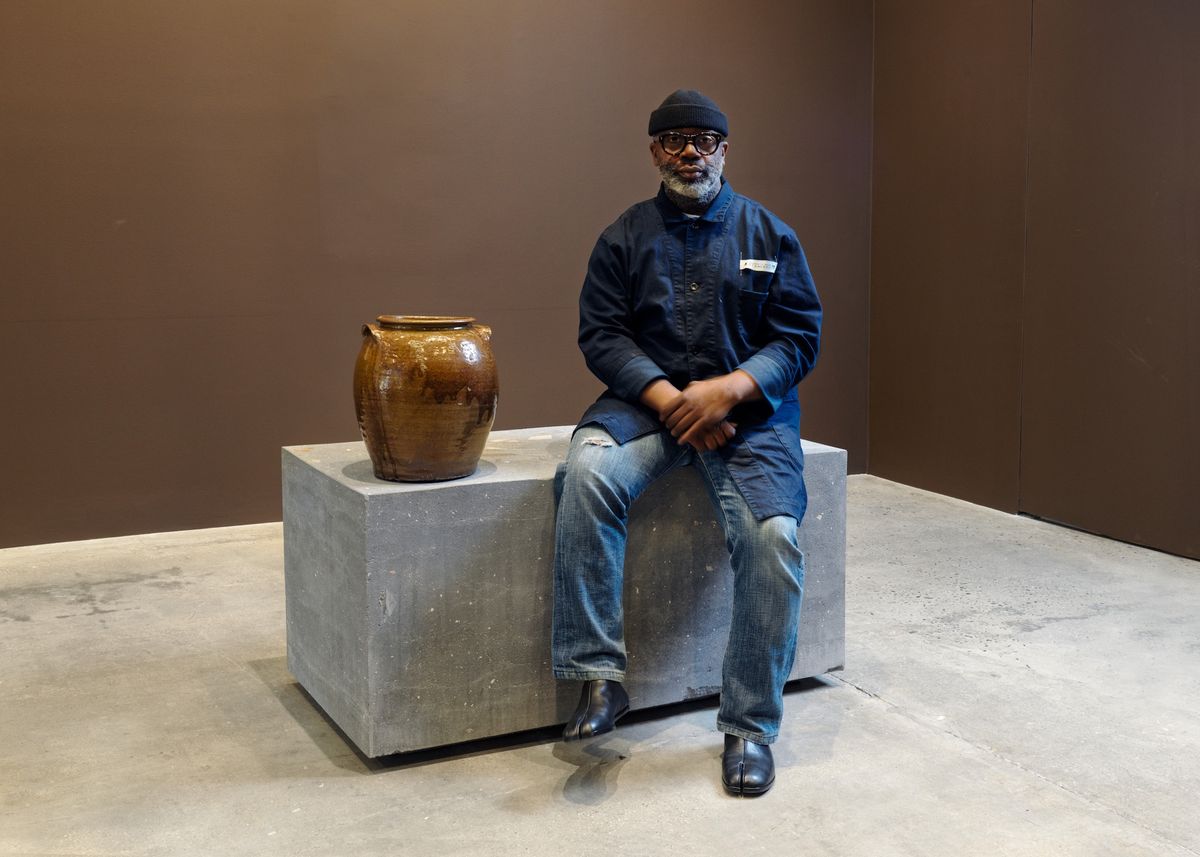 Theaster Gates inside the exhibition, Dave: All My Relations at Gagosian's 821 Park Avenue location in New York, with the historic work by David Drake from his personal collection that he is gifting to Dave's descendants, and seated on a new sculpture he made by pulverizing around 45 of his own pots Photo: Maris Hutchinson