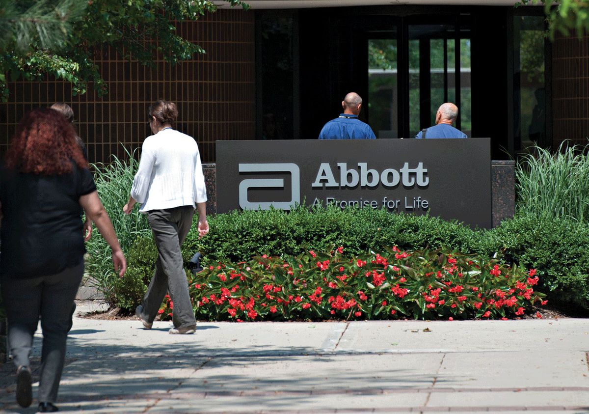 Employees walk near an Abbott Laboratories sign at the company's headquarters complex in Abbott Park, Illinois © Photo: Daniel Acker/Bloomberg via Getty Images