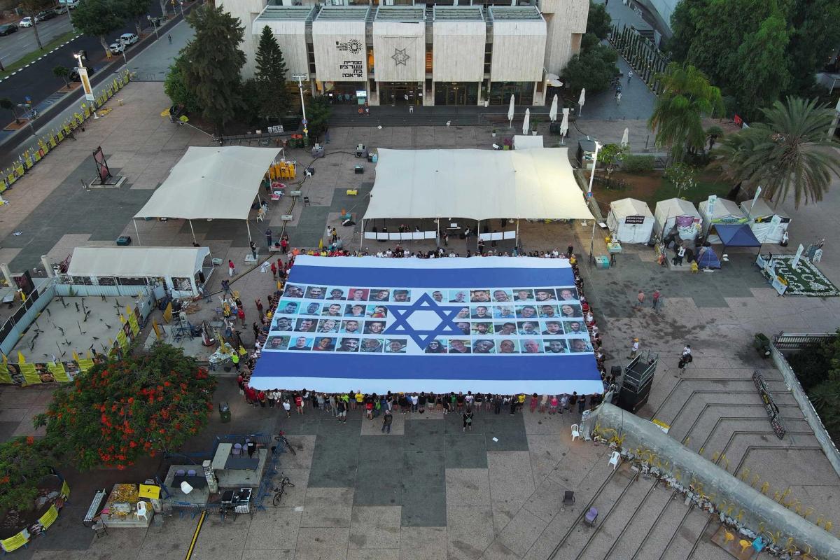 Protesters in Habima Square, also known as Hostages Square, a public plaza located in front of the Tel Aviv Museum of Art, hold up an Israeli flag featuring photos of the hostages held in Gaza, demanding their return

Photo: Yair Palti/Anadolu via Getty Images. © 2025 Anadolu