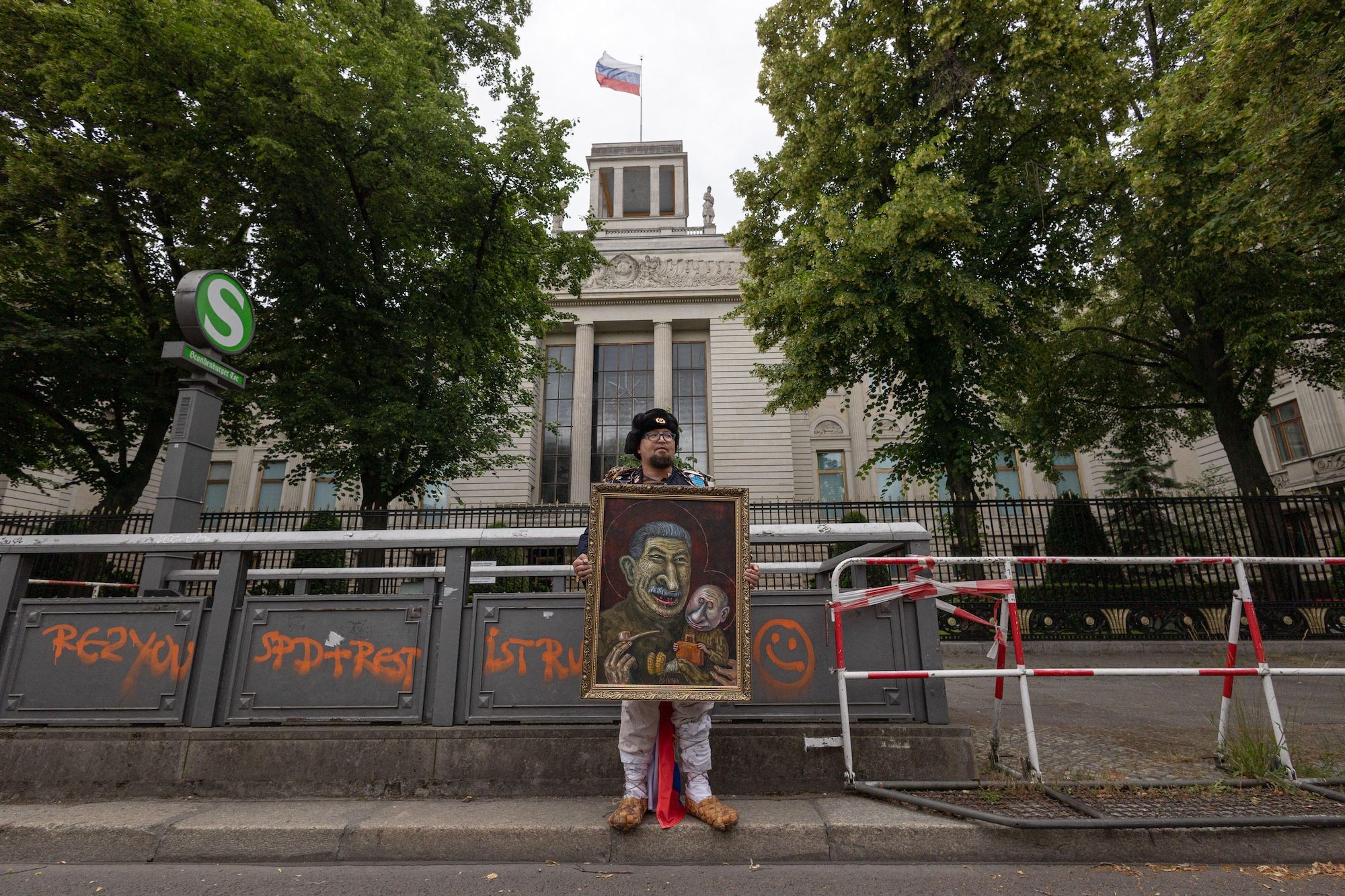 The Russian dissident artist Robert ⁠Kuzovkov (who went by the pseudonym Semyon Skrepetsky) holds one of his satirical paintings outside the Russian embassy in Berlin on 12 June SOPA Images Limited/Alamy Live News