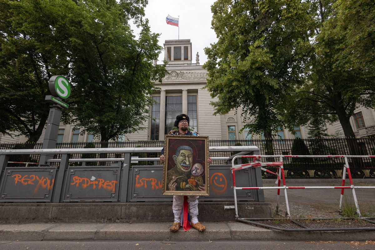 The Russian dissident artist Robert ⁠Kuzovkov (who went by the pseudonym Semyon Skrepetsky) holds one of his satirical paintings outside the Russian embassy in Berlin on 12 June SOPA Images Limited/Alamy Live News