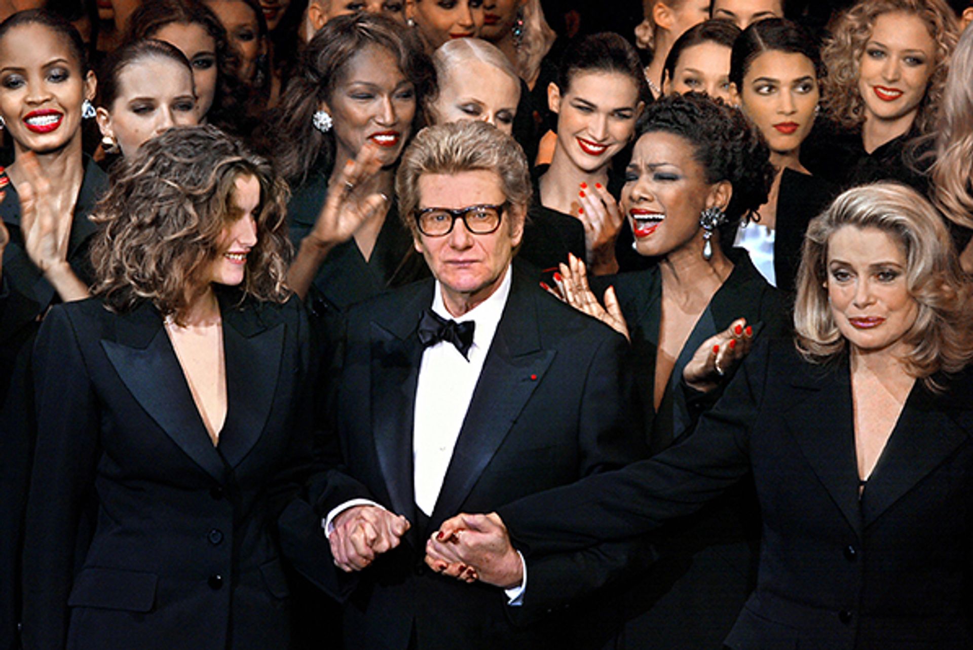 Designer Yves Saint-Laurent with the French model Laetitia Casta (left) and the French actress Catherine Deneuve (R) at his last ever haute-couture show in 2002 © Jean-Pierre Muller/EPA