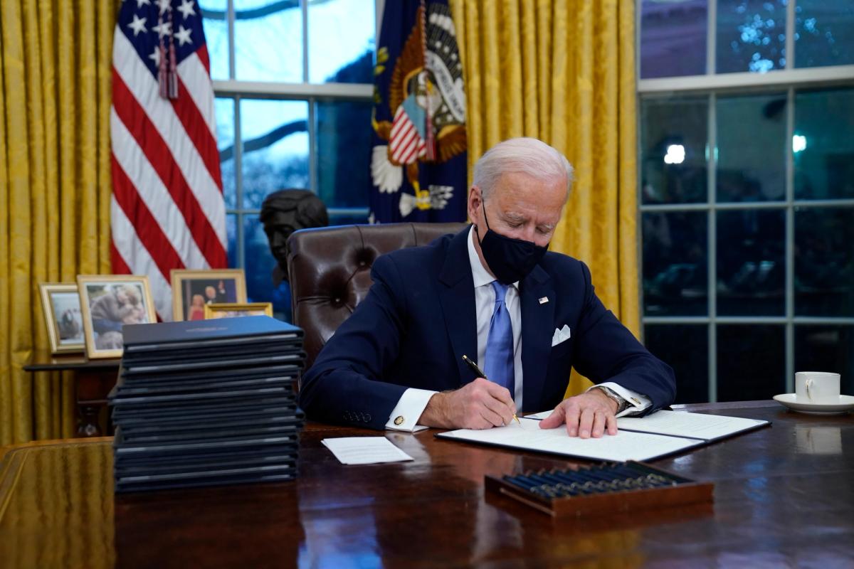 President Joe Biden signs his first executive order in the Oval Office of the White House on 20 January AP Photo/Evan Vucci