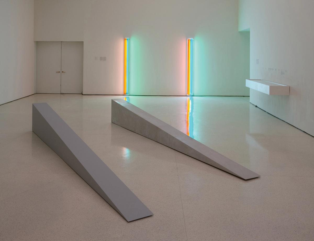 In foreground, two fabrications of Robert Morris's Untitled (Door Stop), 1965. (On left: 2018 artist-supervised, museum-made plywood fabrication; on right: 1965 fiberglass fabrication).  On far wall: two fabrications of Dan Flavin's Untitled (to Henri Matisse) 1964. (On left: historical fabrication received from Panza; right: 1995 fabrication produced in coordination with the Flavin studio) David Heald/© Solomon R. Guggenheim Foundation, New York