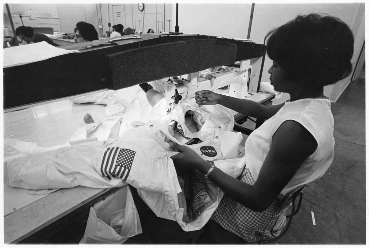 "Sewing a Fine Seam—Finishing touches are applied to one section of the new spacesuit for NASA's Apollo lunar missions on this long-arm sewing machine, built specially for manufacturing the spacesuits." Hazel Fellows, seated, machine-sewing pieces of an Apollo A7L spacesuit on the production line at International Latex Corporation (ILC), Federica (Dover), Delaware; released August 9, 1968 Courtesy the Smithsonian National Air and Space Museum, Washington, DC