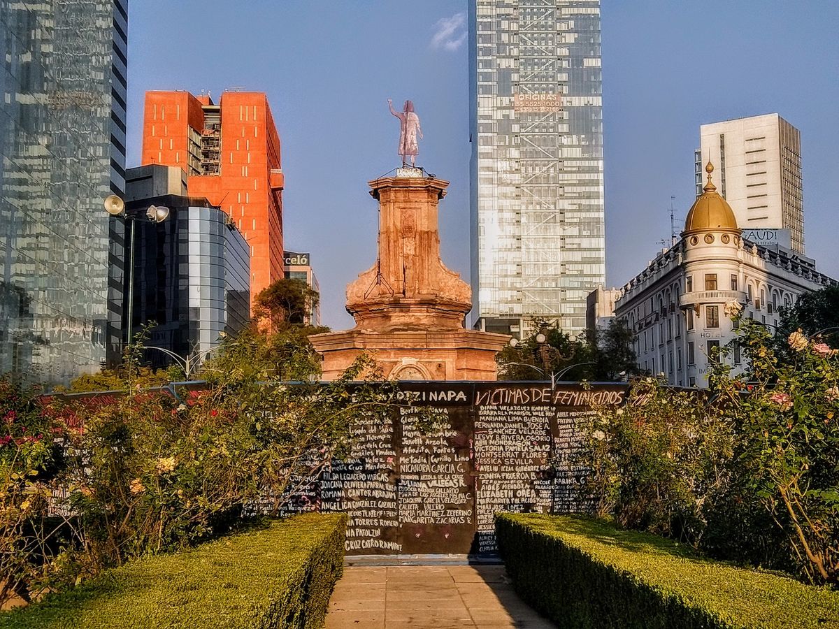 The anti-monument and protest signage at the Glorieta de las mujeres que luchan traffic circle. The names of victims of gender violence have been written on the surrounding barriers. Photo by Luisalvaz, via Wikimedia Commons