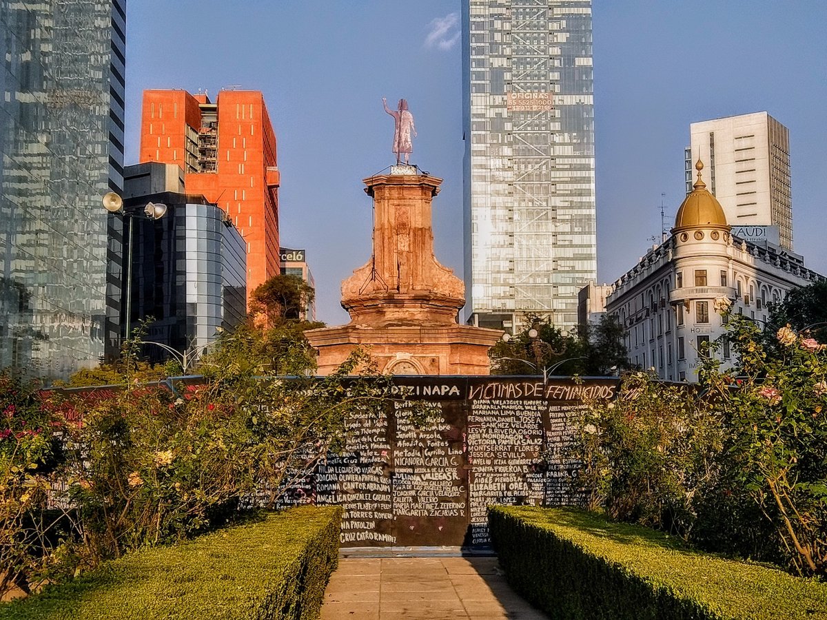 The anti-monument and protest signage at the Glorieta de las mujeres que luchan traffic circle. The names of victims of gender violence have been written on the surrounding barriers. Photo by Luisalvaz, via Wikimedia Commons