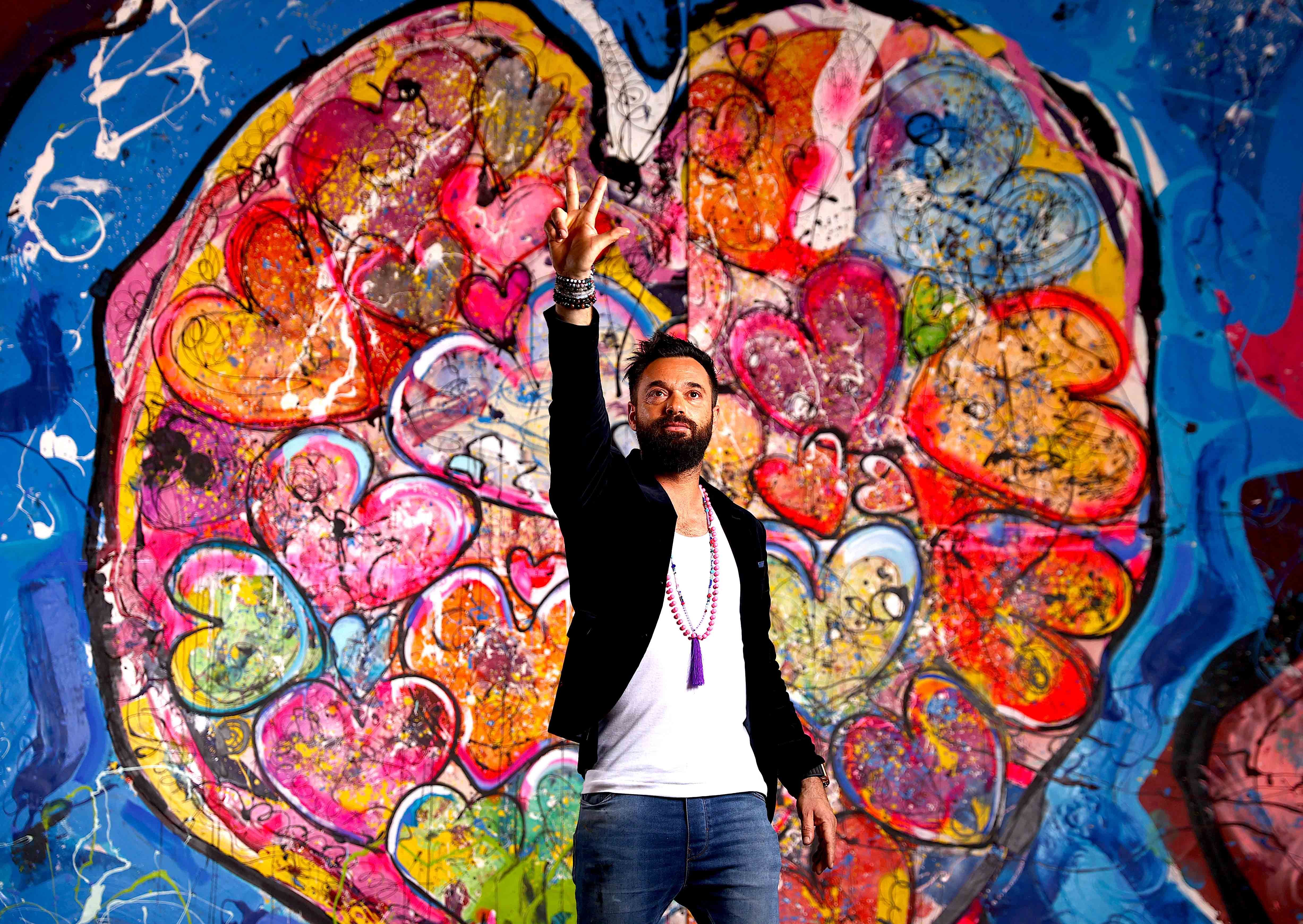 Sacha Jafri in front of the painting that contains Will Smith's handprints, titled The Journey of Humanity—With Love we are Reconnected, Inspired, Re-Energized Courtesy of Sacha Jafri