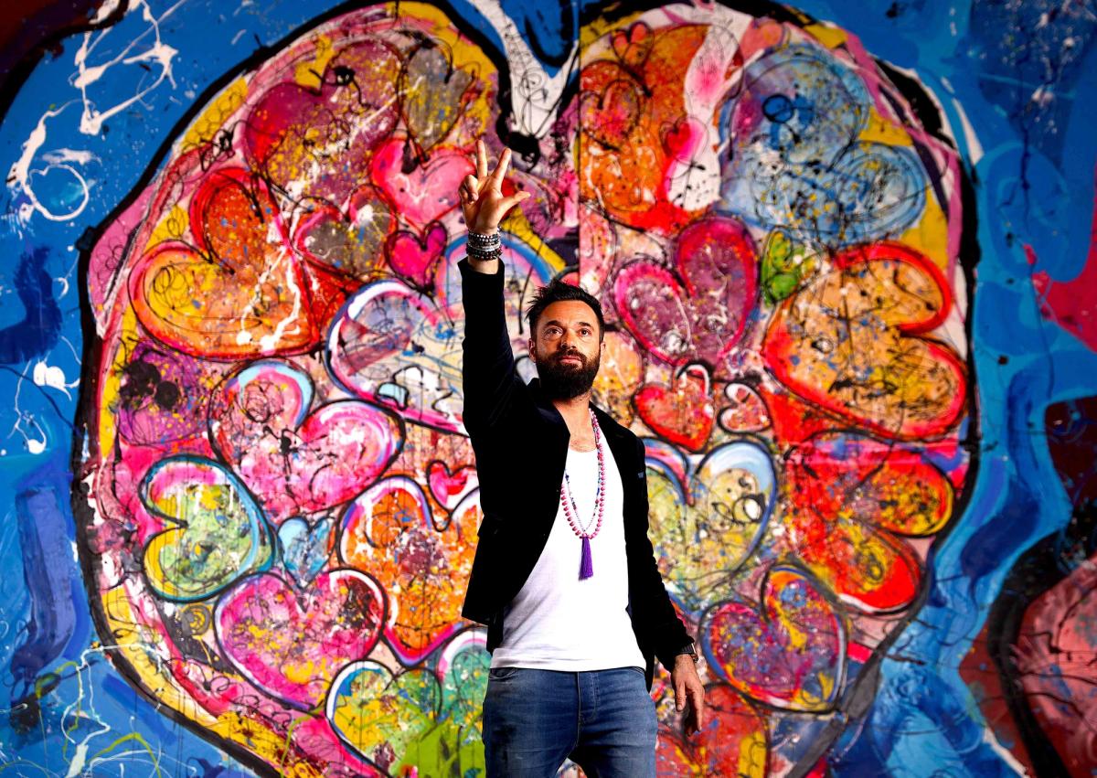 Sacha Jafri in front of the painting that contains Will Smith's handprints, titled The Journey of Humanity—With Love we are Reconnected, Inspired, Re-Energized Courtesy of Sacha Jafri