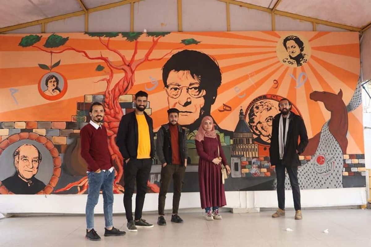 Students and teachers at the Dar al Kalima Training Centre stand in front of a mural at the Gaza art school