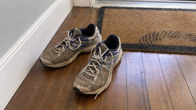 A pair of fresh sneakers by a sunlit doorway with a spray bottle nearby