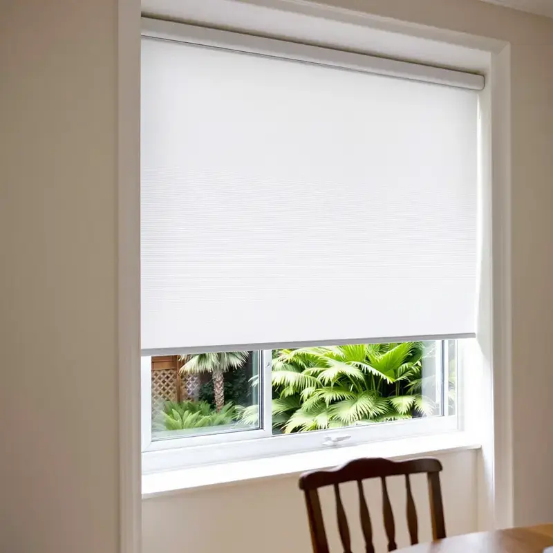 White honeycomb cellular blind lowered over a dining-room window, subtropical New Zealand garden beyond.