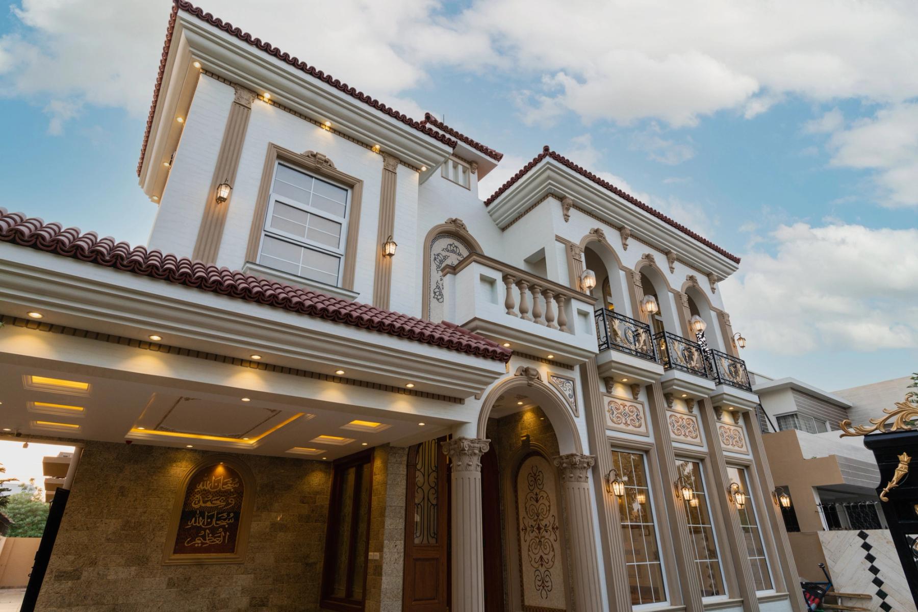 A Mediterranean-revival villa with arched loggias, carved stone columns, a barrel-tiled roof, and a lantern-lit ornamental facade.