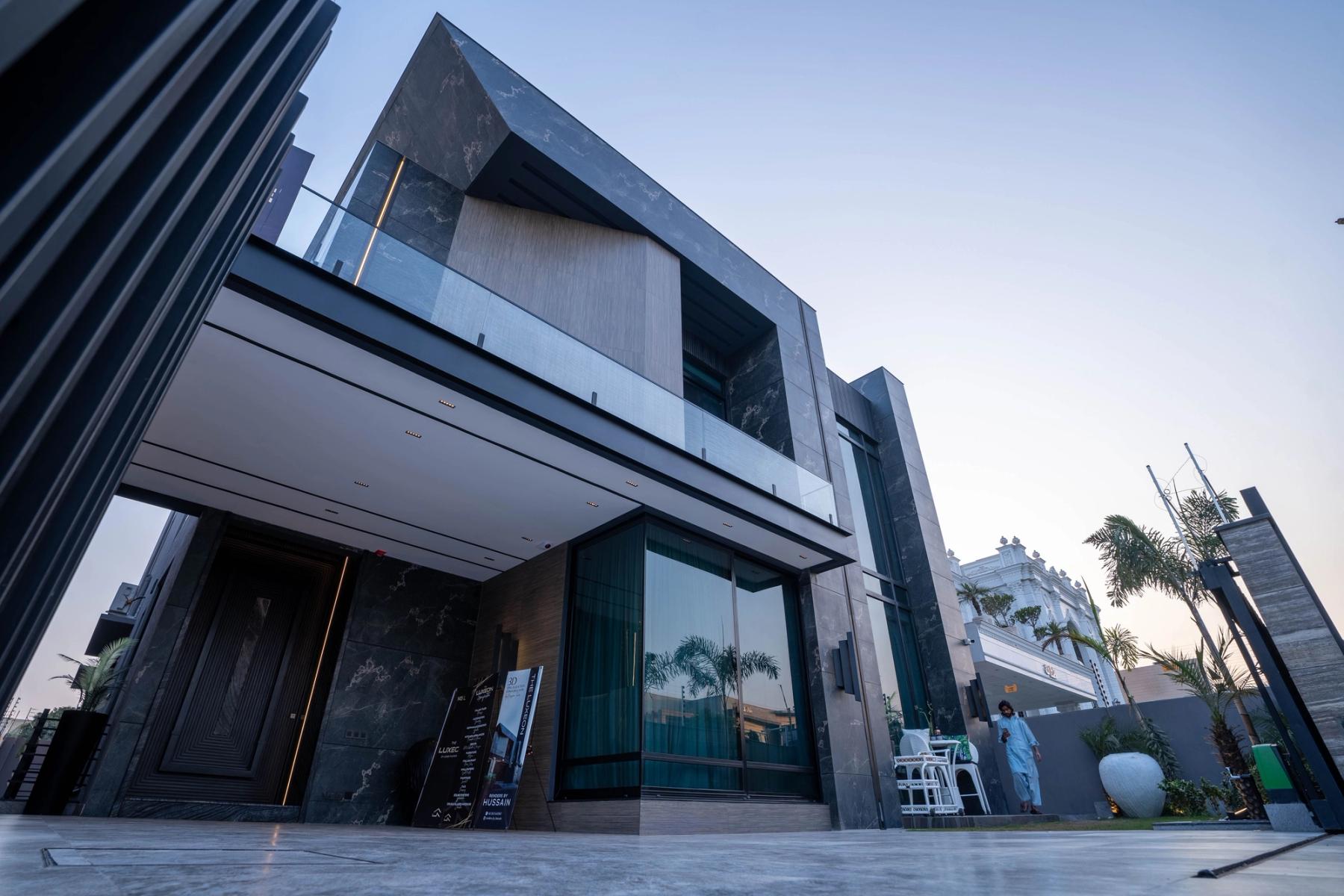 A dark marble-and-glass contemporary villa with a cantilevered upper storey and a full-height glazed entry framed by palms.