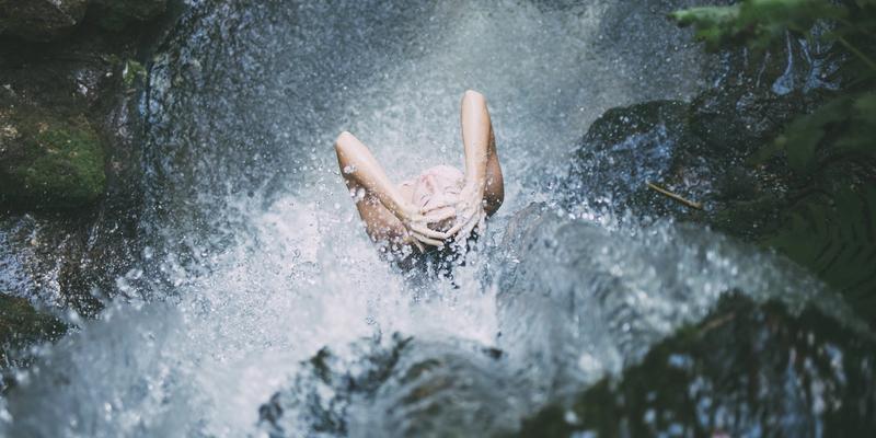 Frau steht unter einem Wasserfall