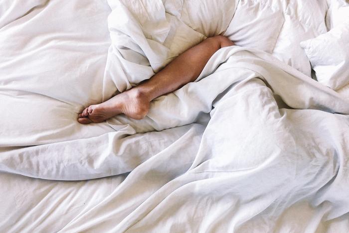 Mensch im Bett mit weißen Laken