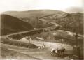 View of the Vera district of Tbilisi with a cross monument, winding road, bridge, and surrounding hills.