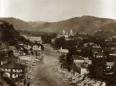 View of Kutaisi with a river flowing through the city, stone bridge remains, residential houses, and a church complex in the background.