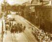 Gelatin silver photograph showing a public street procession with marching participants and gathered spectators in an urban setting during the early 20th century in Georgia.
